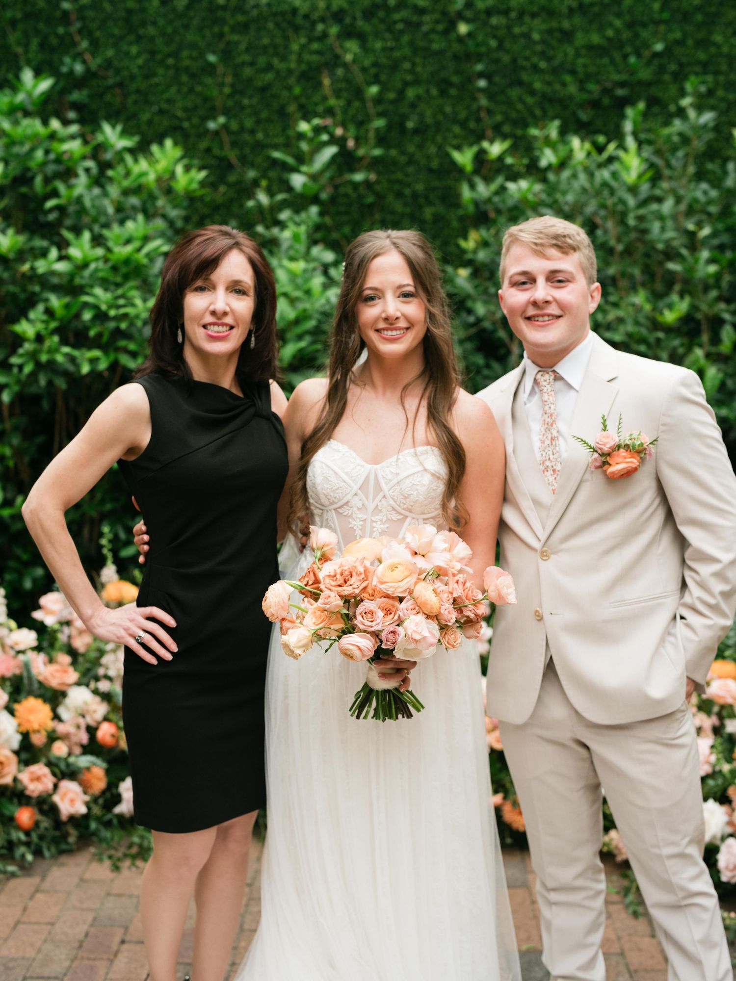 Wedding portrait with floral decor and peach roses against green garden backdrop.