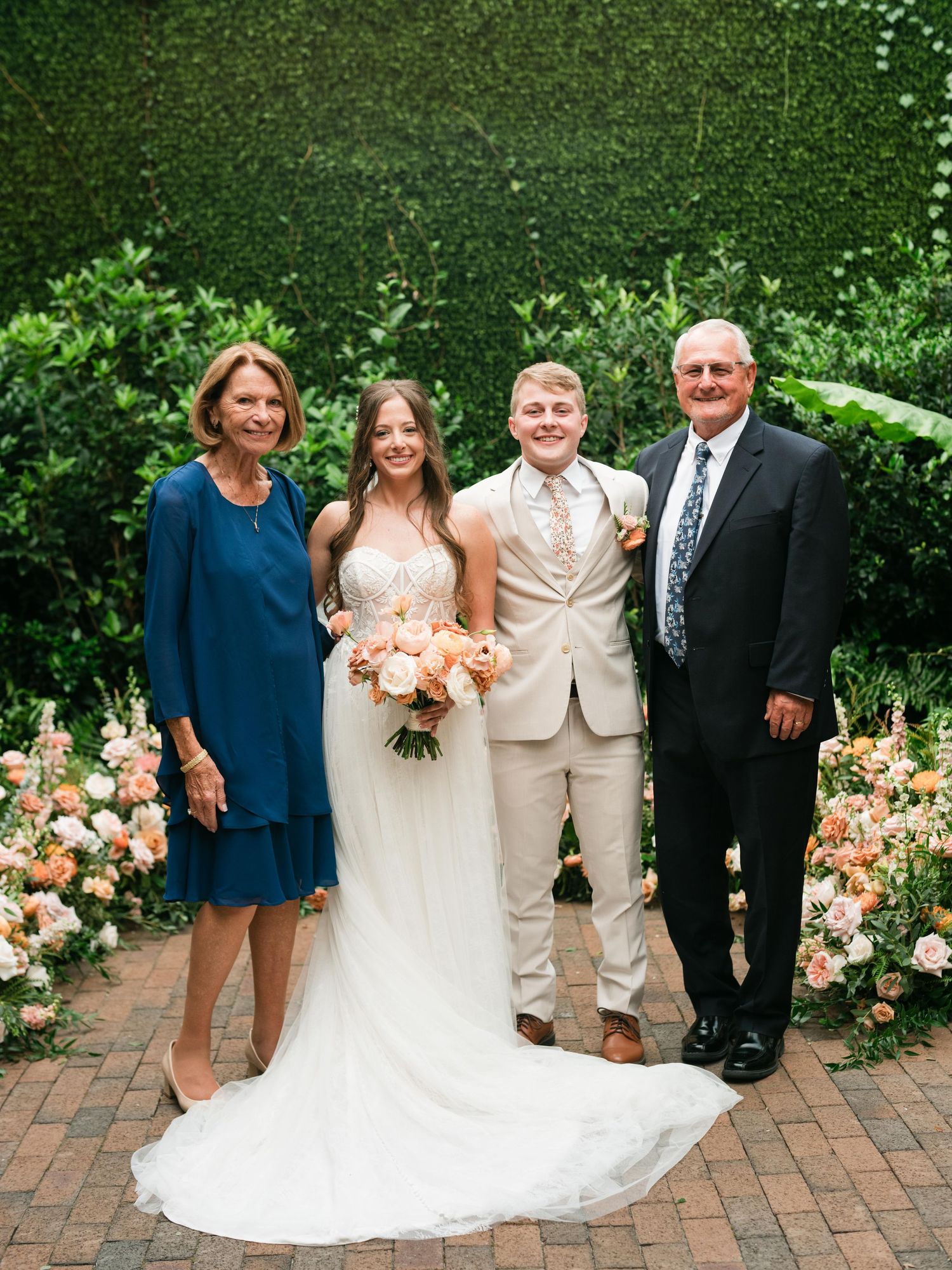 Wedding group photo on brick pathway with peach rose garden backdrop.