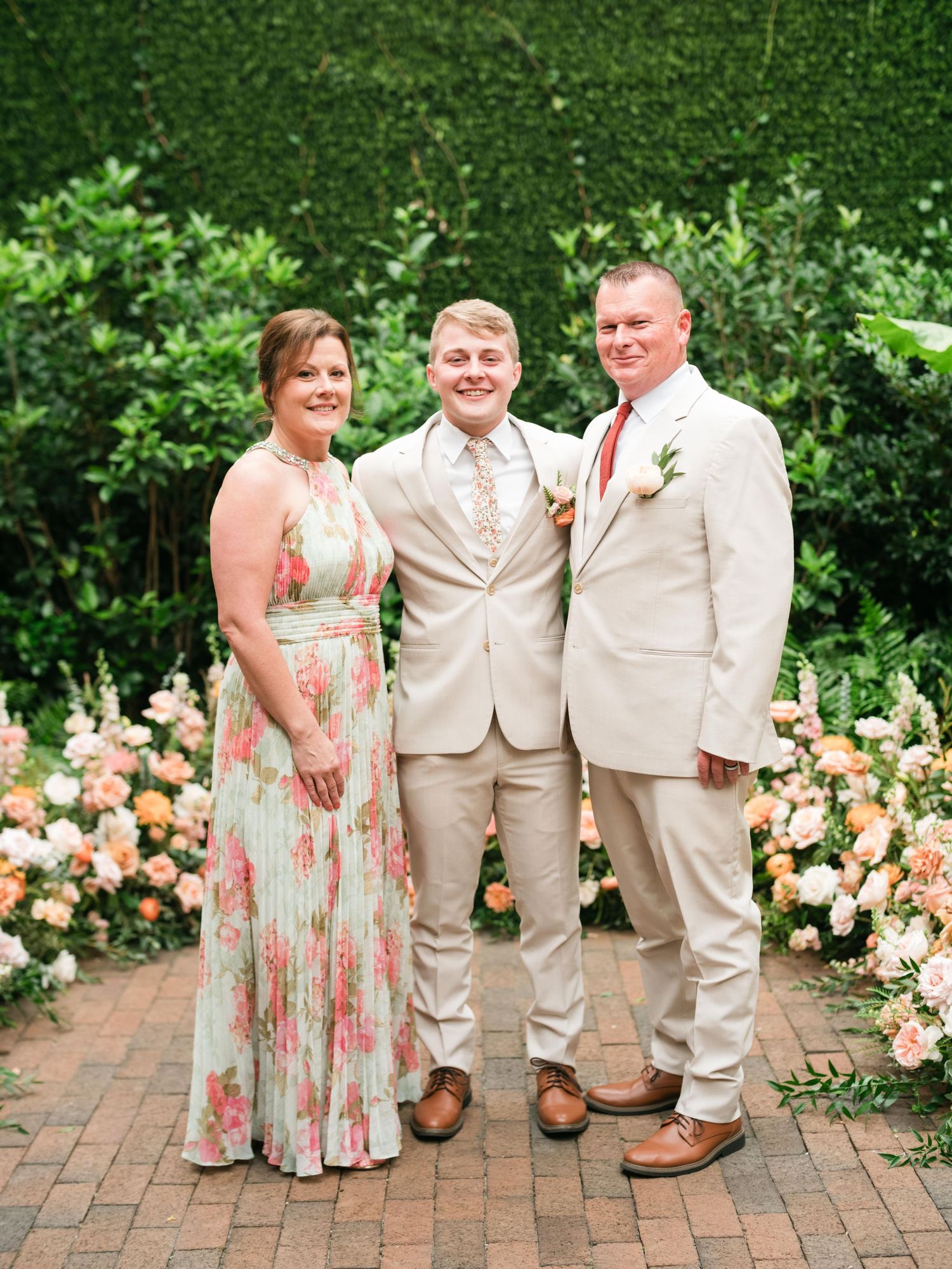 Family group photo in beige and floral attire against garden backdrop.