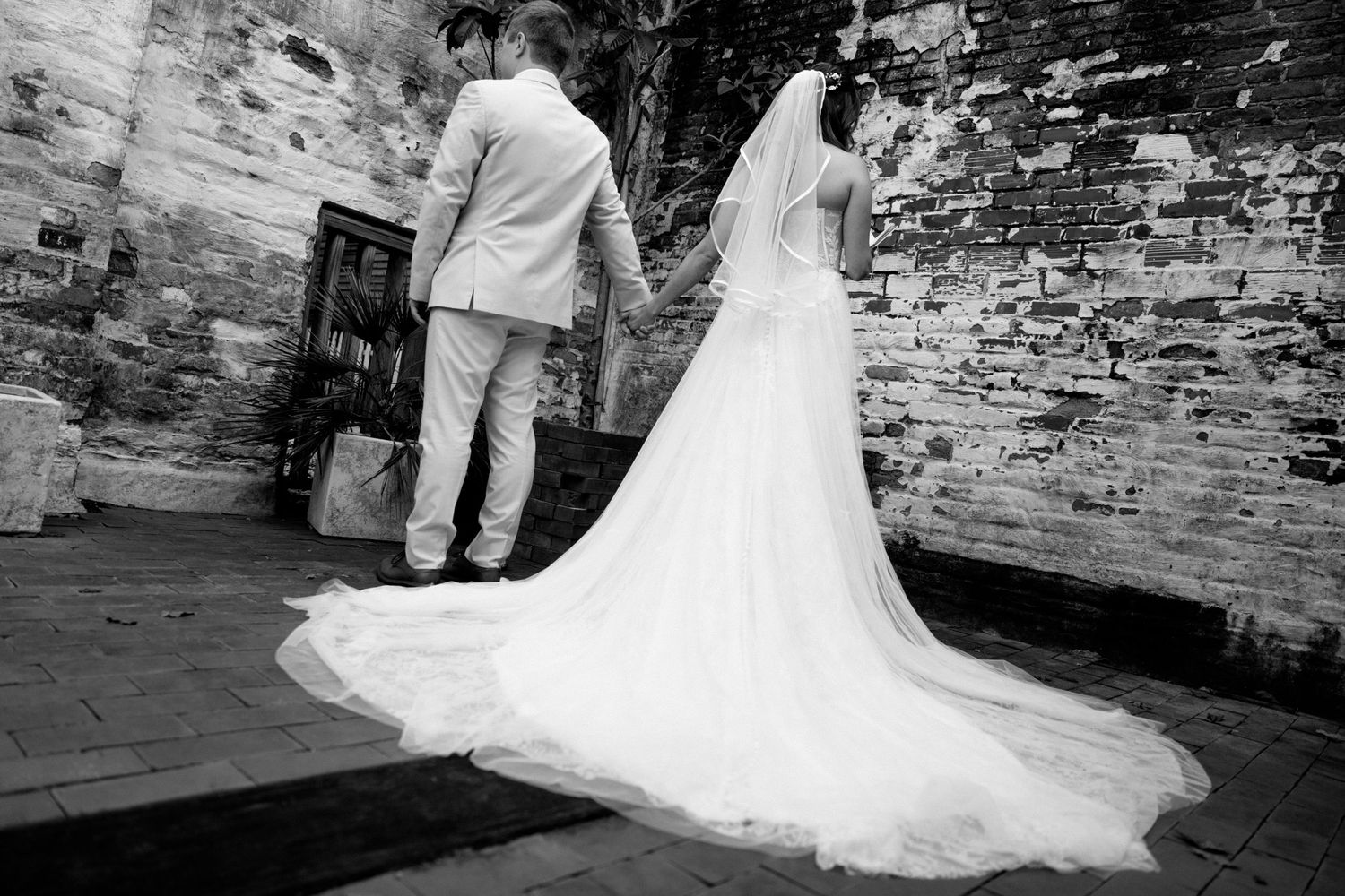 Black and white photo of couple in wedding attire against textured brick wall.