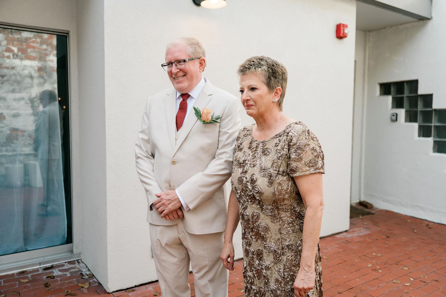 Formal wedding guests in beige and patterned attire pose in modern interior.