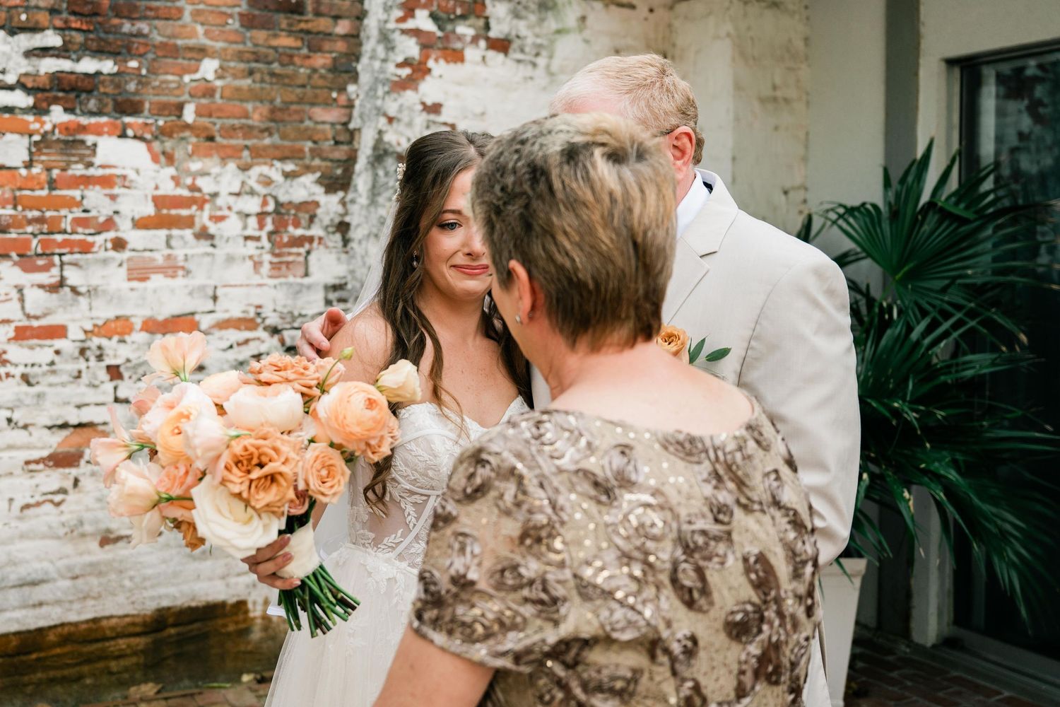 A soft candid moment during an outdoor wedding ceremony against an exposed brick wall backdrop.