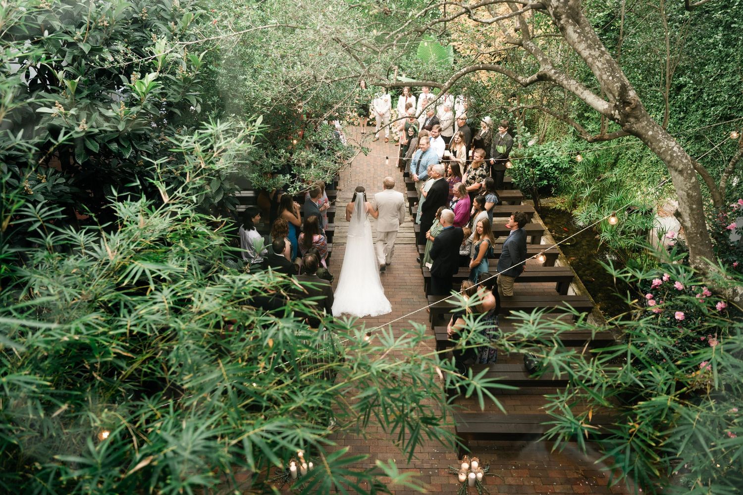 Aerial view of outdoor garden wedding ceremony with guests seated along pathway.
