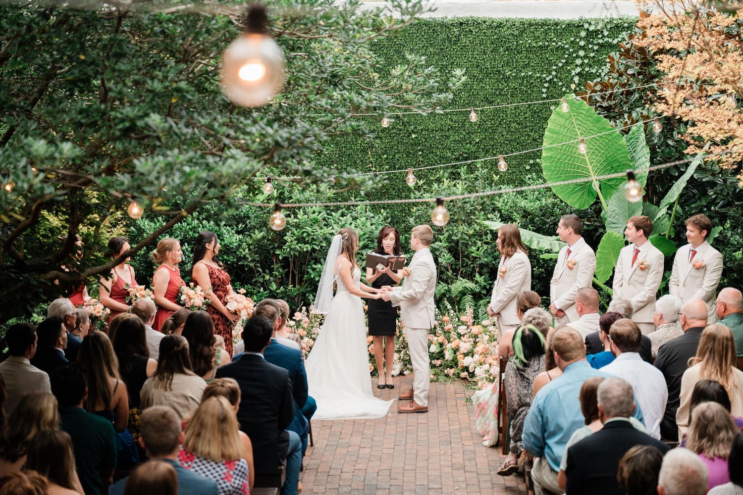 Wedding ceremony in a courtyard garden setting with string lights and florals decorating the space.
