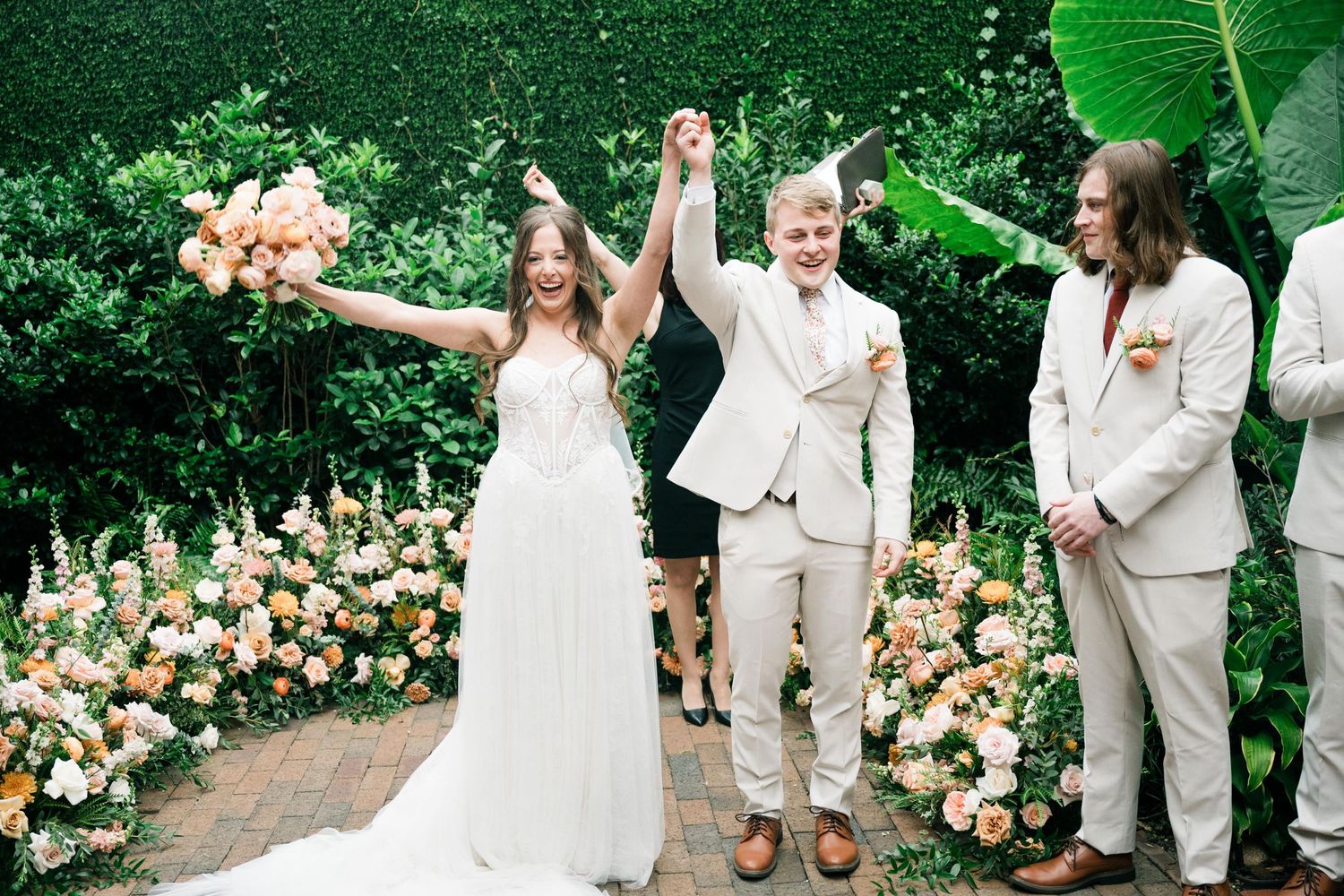 A joyful wedding celebration moment in a garden with peach floral arrangements and green foliage backdrop.
