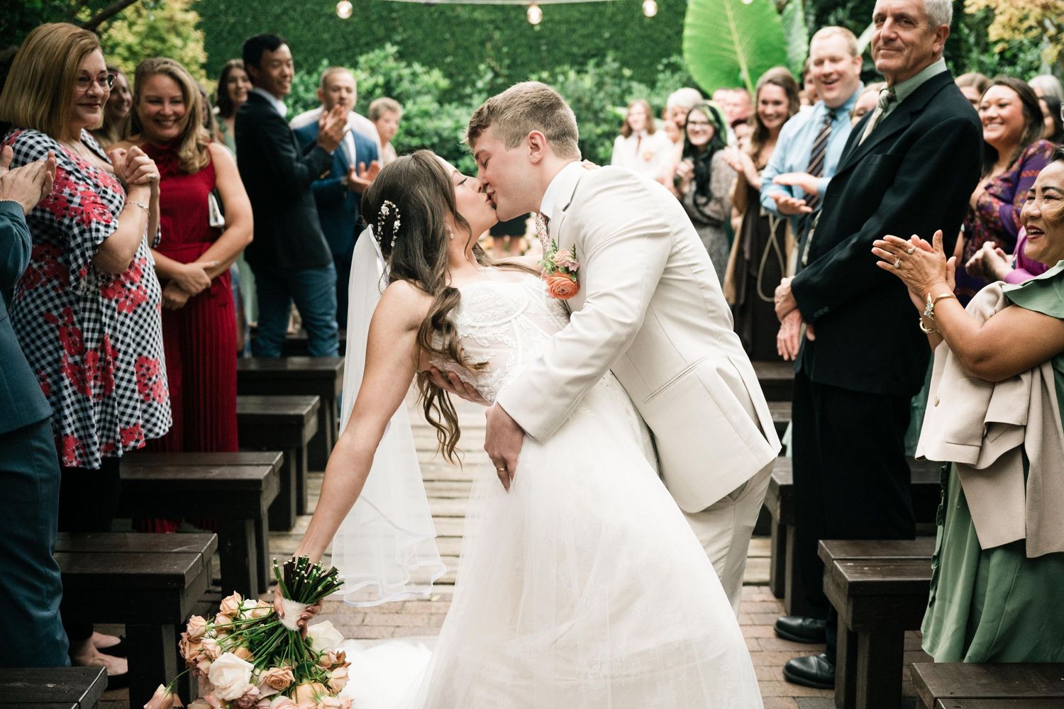 A romantic dip kiss moment during a wedding ceremony surrounded by guests.