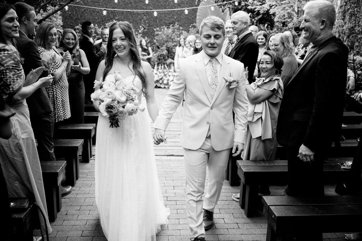 A couple walks down the aisle at their wedding ceremony while guests celebrate with applause.