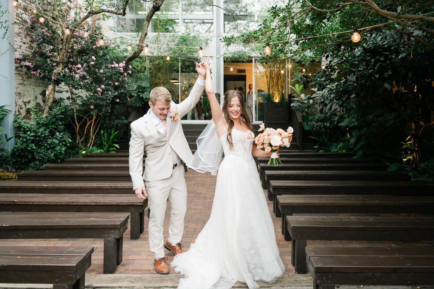 Newlyweds celebrate joyfully while walking down wooden steps at an outdoor garden wedding ceremony venue.