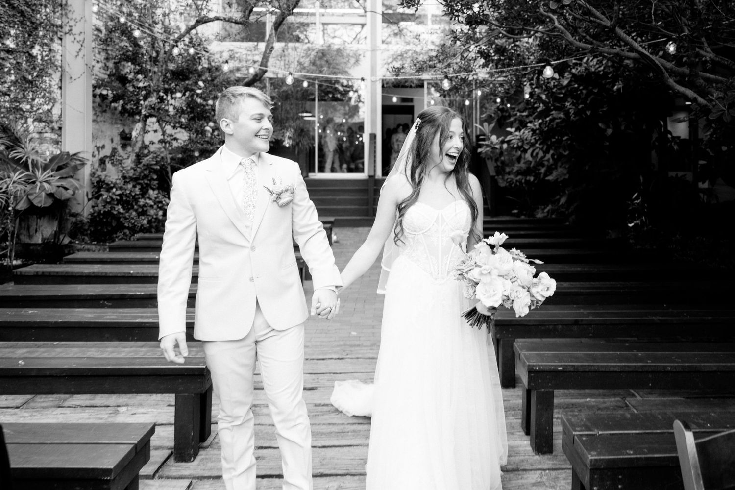 A couple holding hands during their wedding ceremony in a garden setting in black and white.