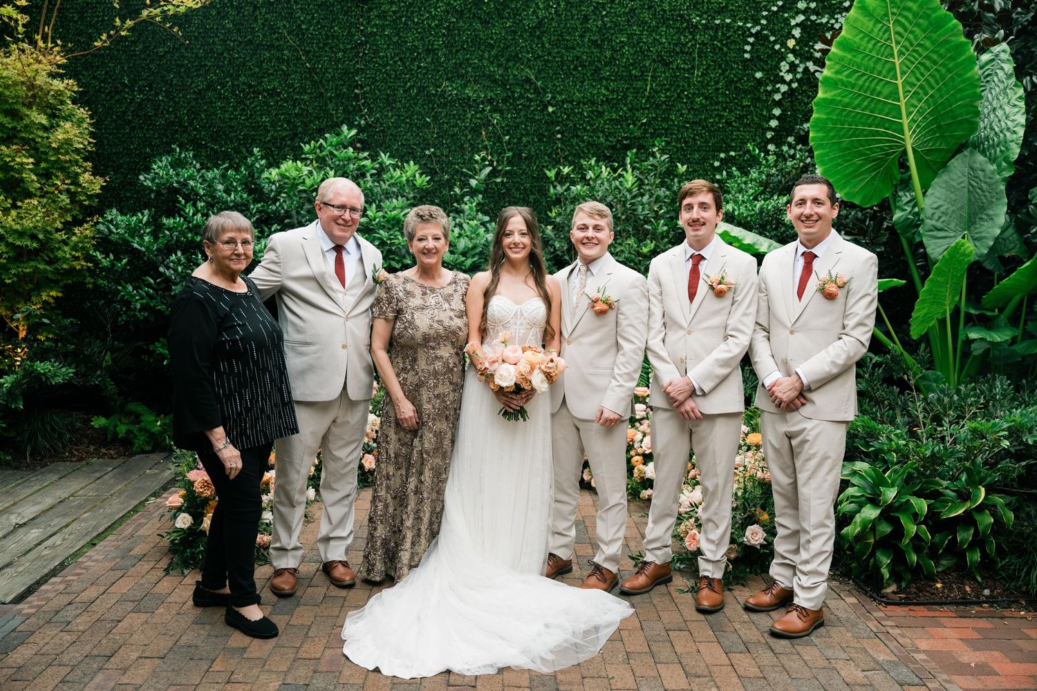 Wedding party poses on a brick pathway with lush greenery and tropical plants in the background.