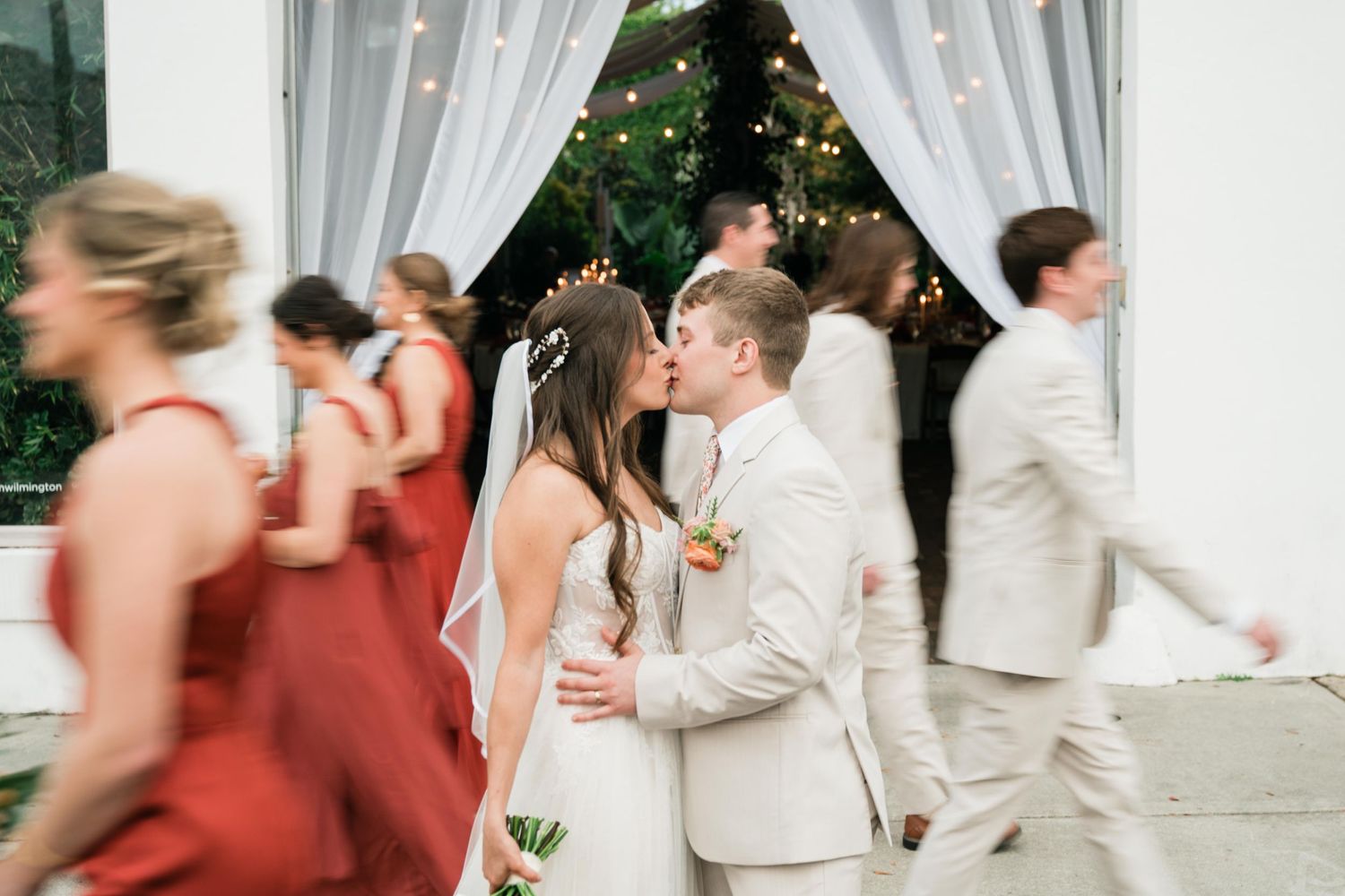 Wedding guests in movement during reception as they pass by flowing white curtains and string lights.
