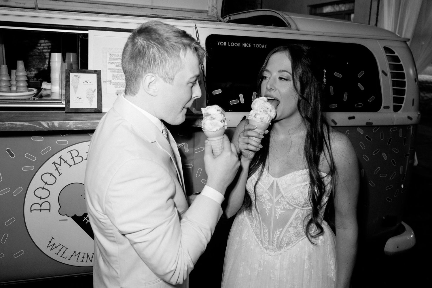 A black and white photo of two people enjoying ice cream cones together at an outdoor food stand.