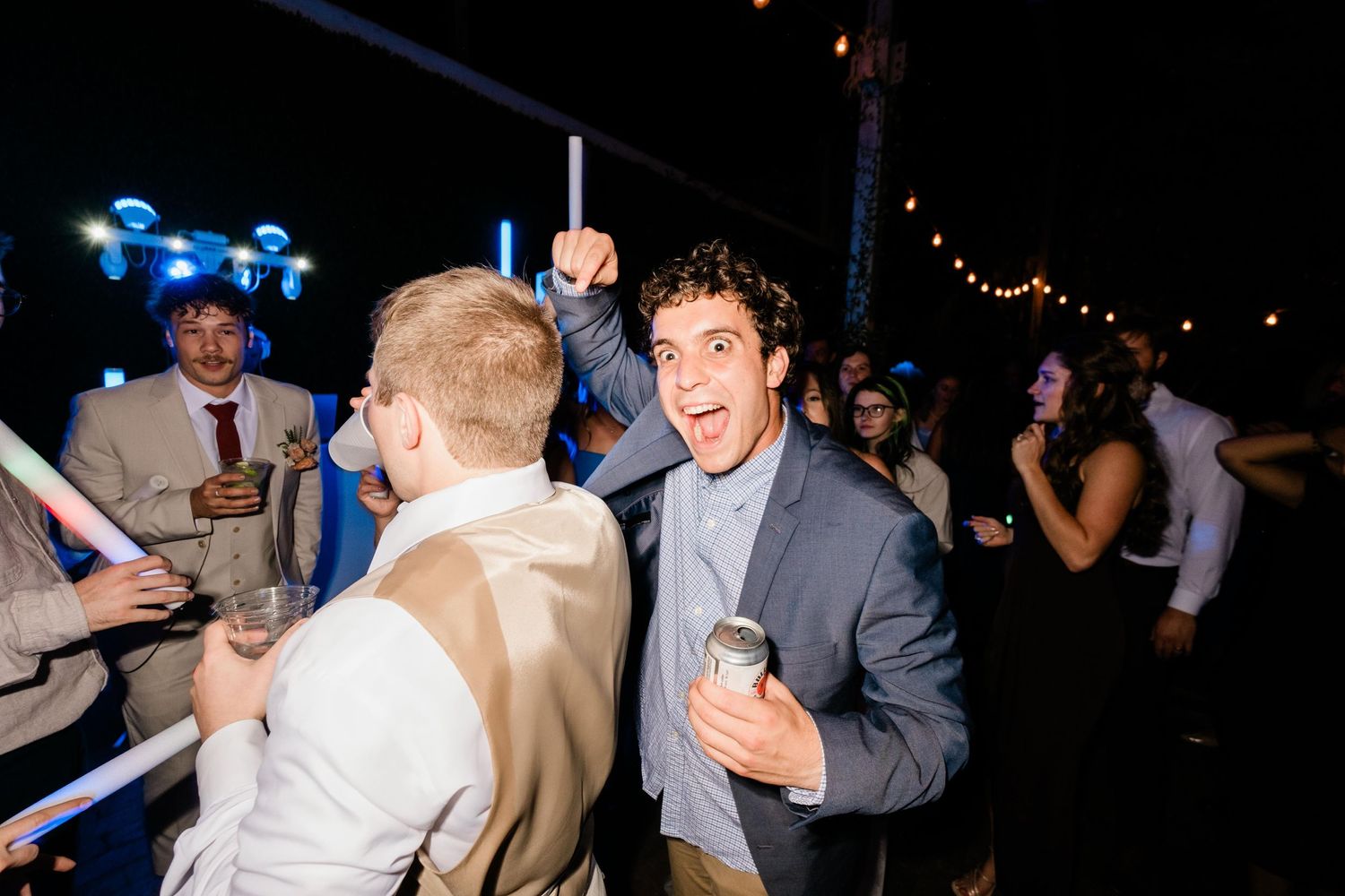 Two people share an enthusiastic moment while dancing at a nighttime celebration with blue glowsticks visible in background.