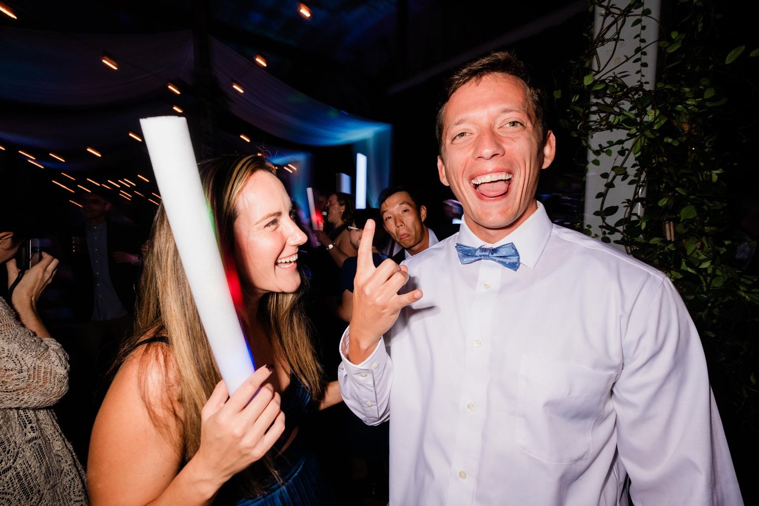 People celebrating at a nighttime party with someone holding a diploma scroll and wearing a bowtie.