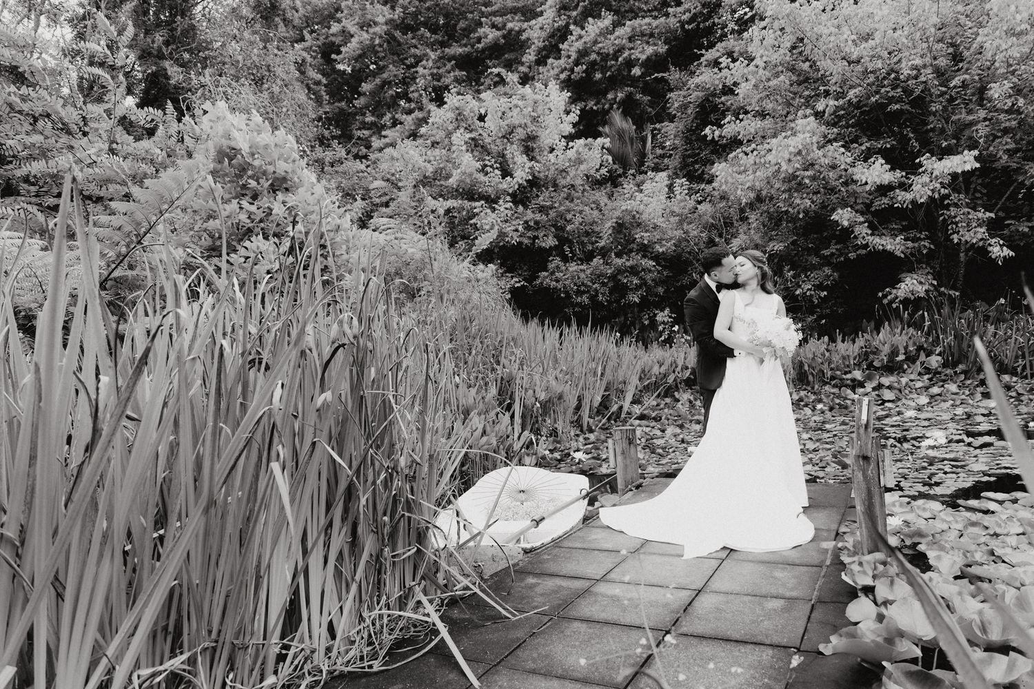 A black and white photograph showing the bride and groom near a pond captured by Apertured Media Auckland Wedding Photographer.