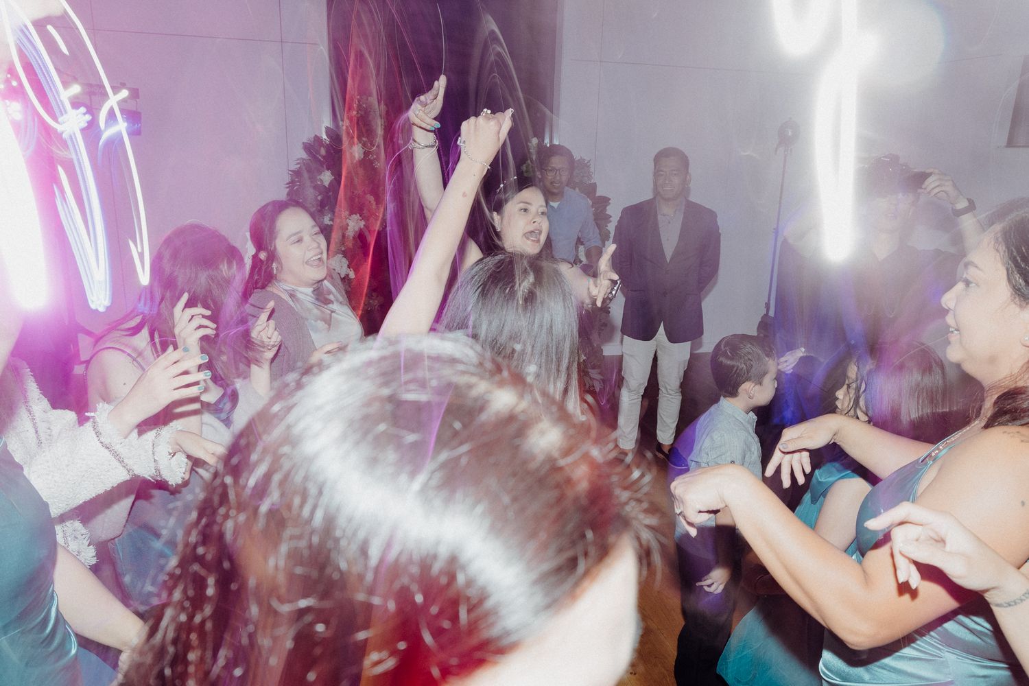 People dancing and socializing at a crowded party with pink lighting captured by Apertured Media Auckland Wedding Photographer.