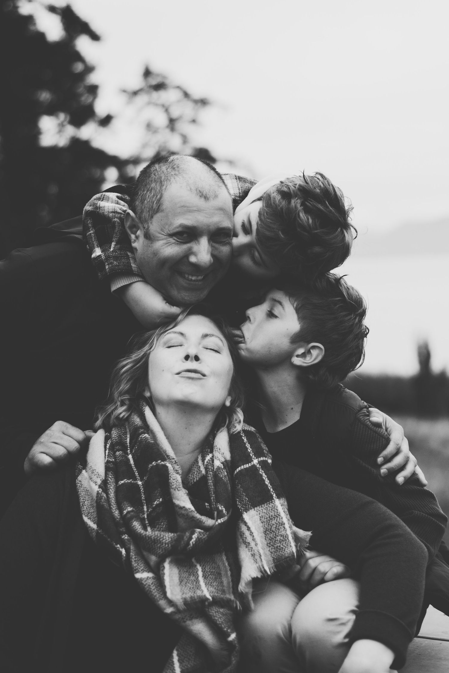 A close black and white portrait of a family sharing a warm embrace and laughter outdoors.