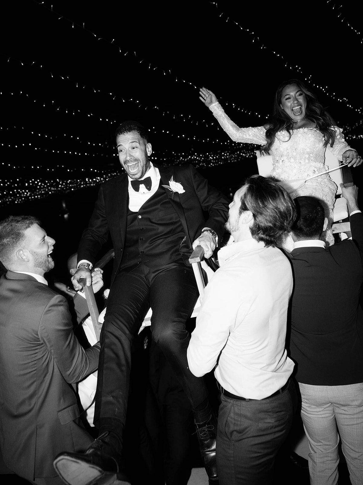 Wedding guests celebrate and dance under twinkling string lights during a lively reception party.