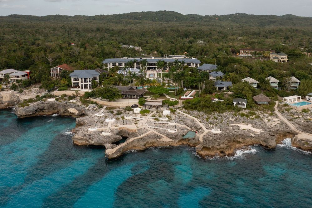 Aerial view of luxury oceanfront villas perched on rocky cliffs above turquoise Caribbean waters.