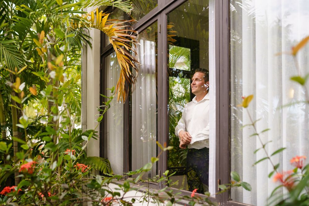 A conservatory window surrounded by lush greenery and tropical plants with someone in white standing inside.