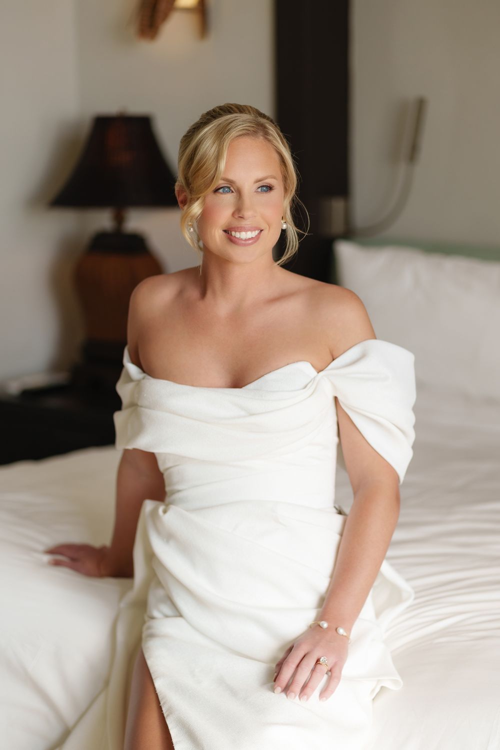 A contemporary wedding dress portrait featuring an elegant off-the-shoulder white gown on a light neutral background.