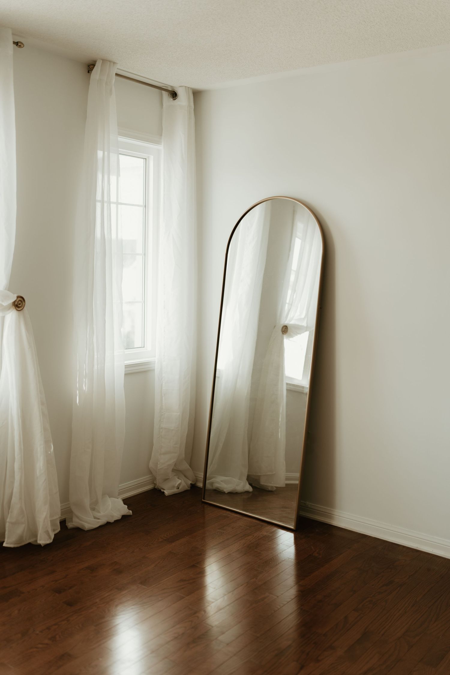 Minimalist room interior with floor length mirror and sheer white curtains.