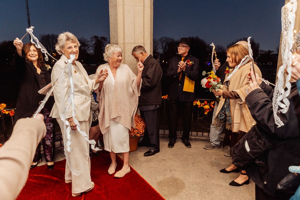 Wedding celebration with guests applauding couple on red carpet under stone archway.