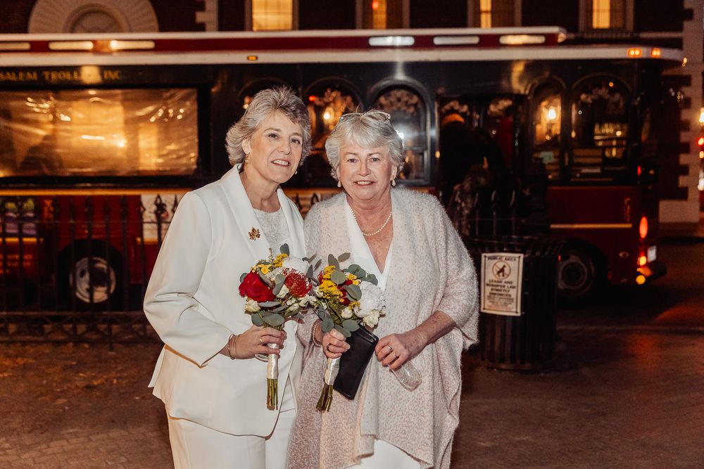 A happy couple holds colorful bouquets while posing together in an indoor venue.