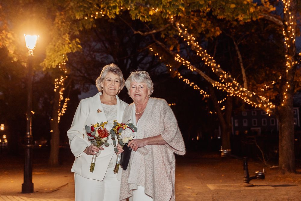 A couple poses with bouquets under trees decorated with twinkling lights at night.