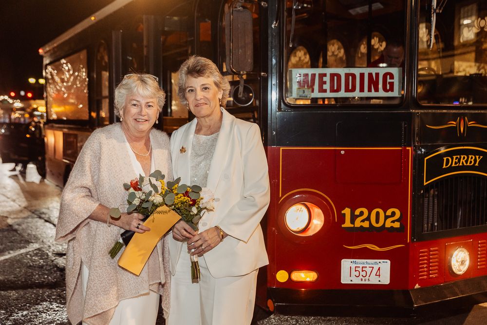 A couple stands in front of a vintage red trolley with a wedding sign at night.