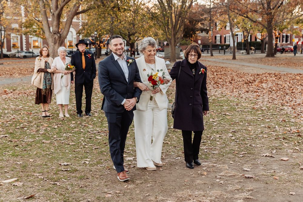 Wedding party walks through fallen autumn leaves during an outdoor ceremony.