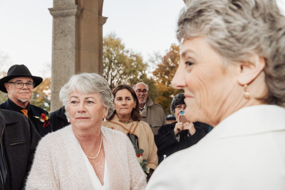 Wedding guests and couple gather beneath stone archway during autumn ceremony.