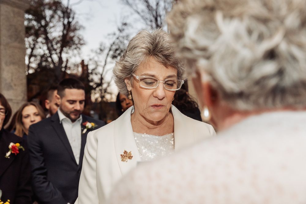 Wedding guests gathering outside with elegant attire and fall foliage in the background.