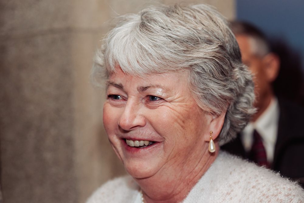 Person smiling warmly while wearing a cream colored sweater at formal gathering.