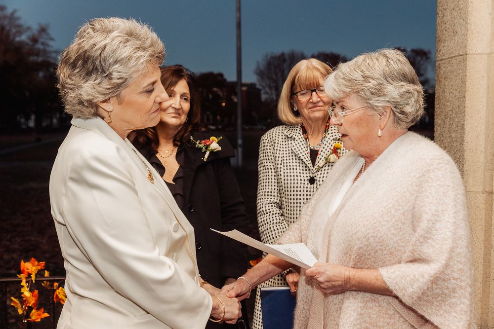 Two people reviewing documents during outdoor ceremony with observers in background.