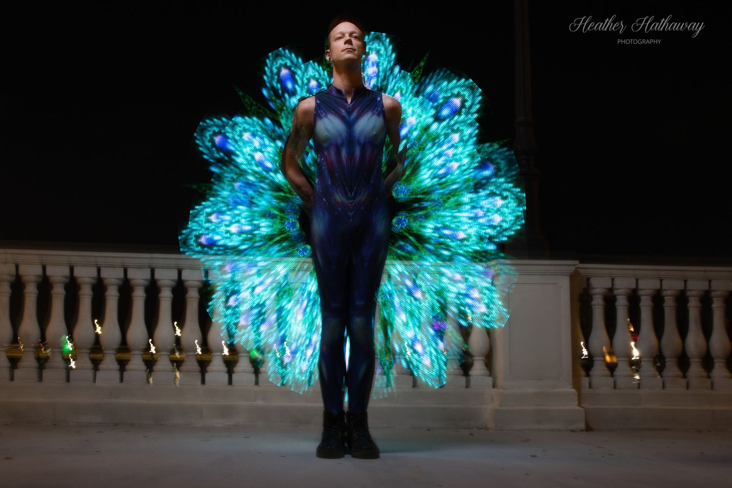 A figure stands illuminated against a dark background with glowing blue-green peacock-style light effects behind them.