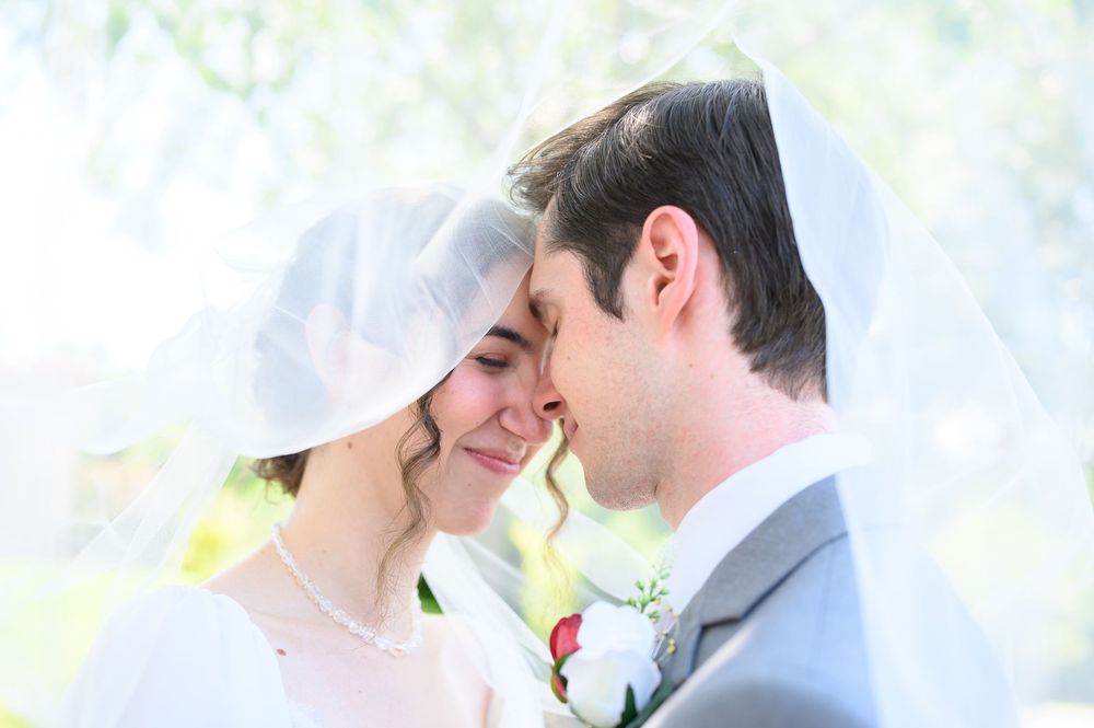 Happy newlywed couple share a close intimate moment together under an umbrella in a garden setting during their wedding.