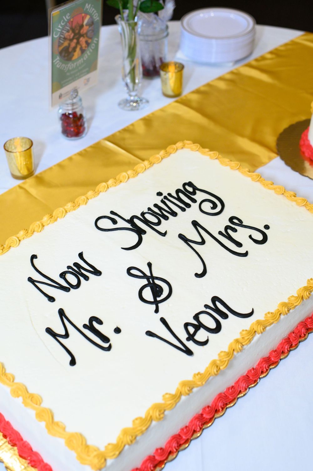 Wedding reception cake features multiple white frosted sheet cakes with yellow border trim displayed on a white tablecloth.