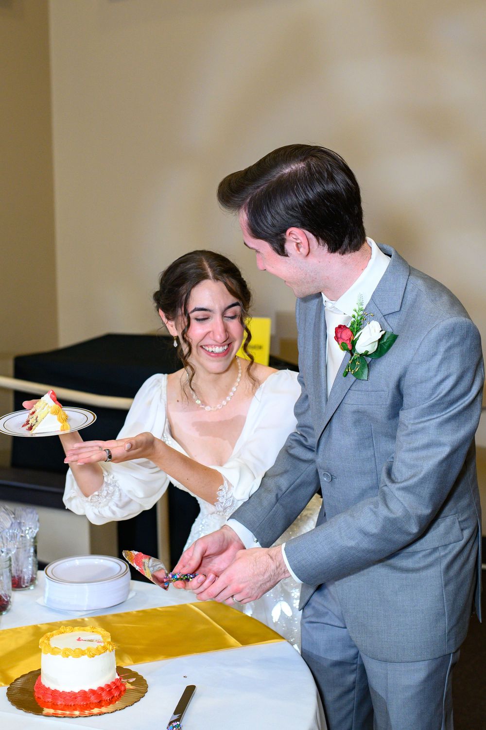 A couple in wedding attire playfully share a slice of cake during their reception celebration.