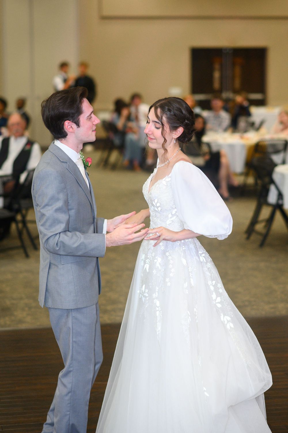 Couple sharing their first dance in a reception hall, bride wearing a flowing white gown.