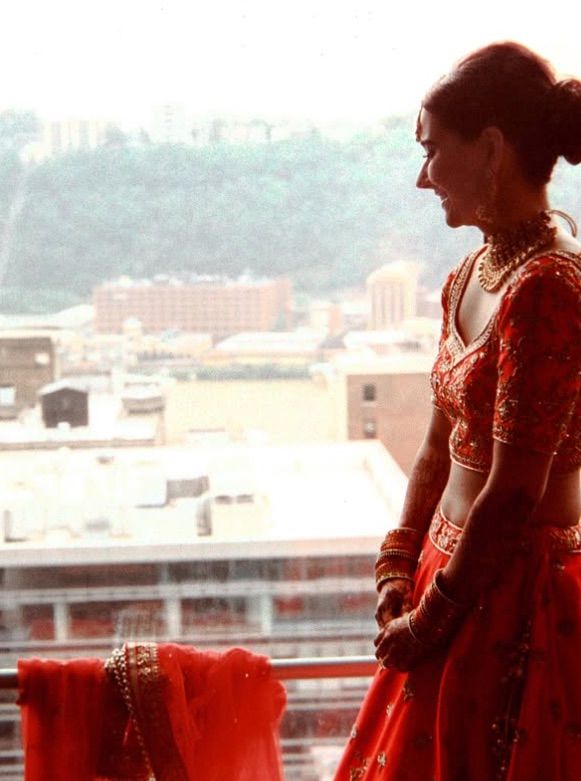 Person in traditional red Indian saree and jewelry stands on balcony overlooking Pittsburgh in soft vintage photo. 35 mm Film Photography