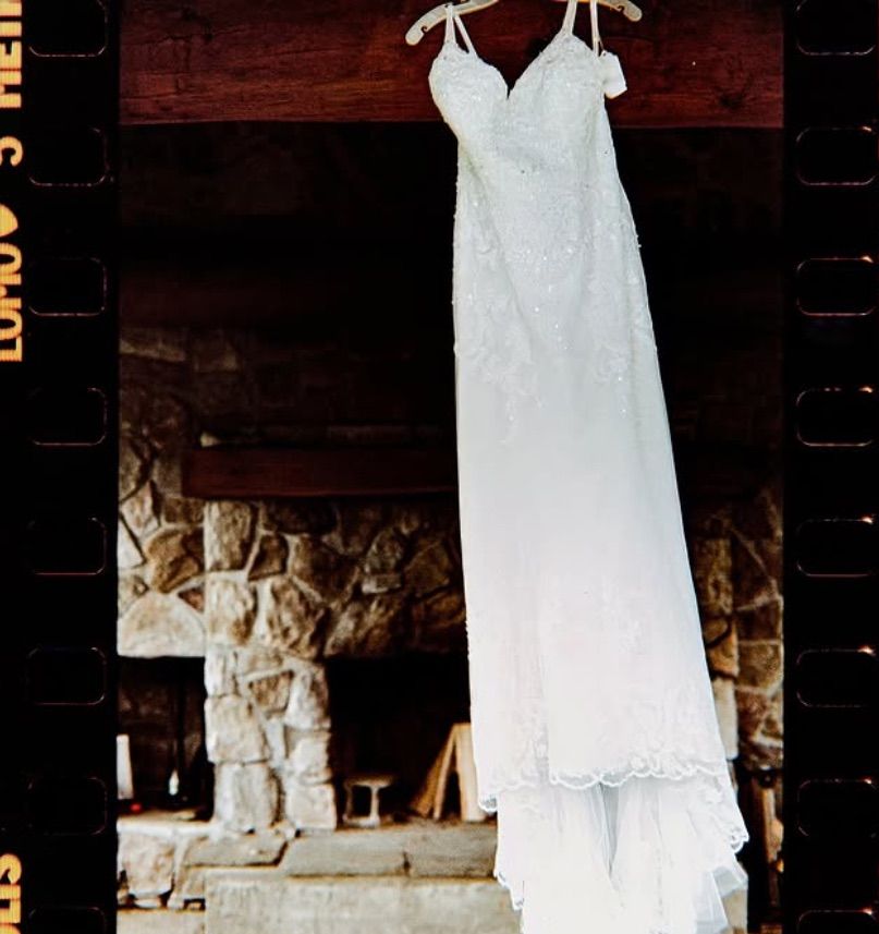 White vintage-style dress hanging against dark wood wall with delicate lace trim details and spaghetti straps. 35 mm Film Photography.