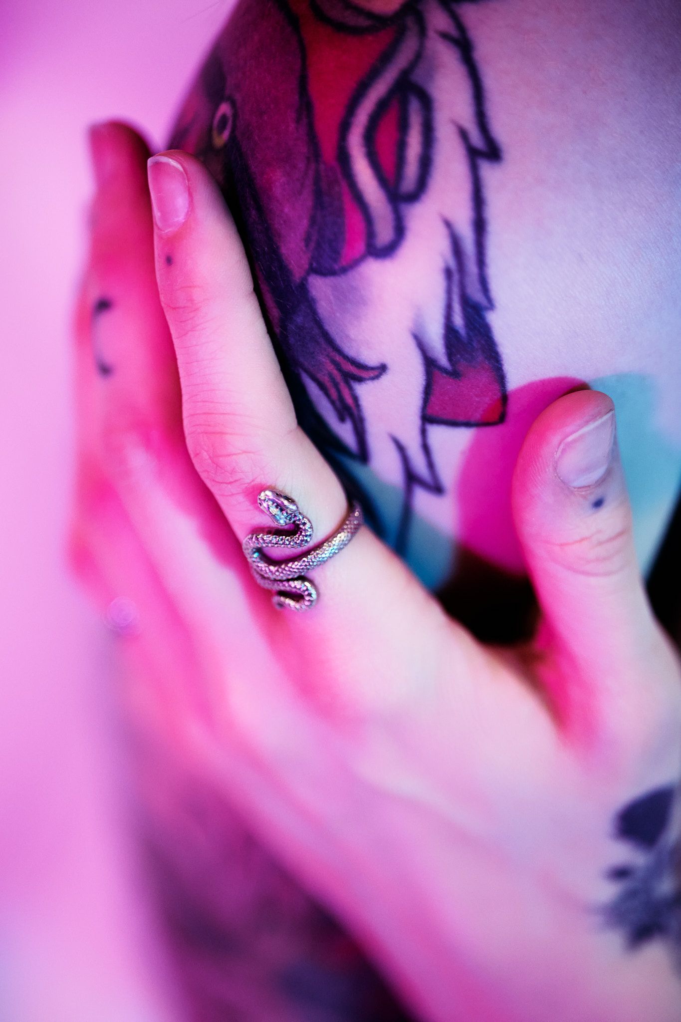 Close-up of a hand with a silver snake ring against a pink and purple background with blurred dark patterns.