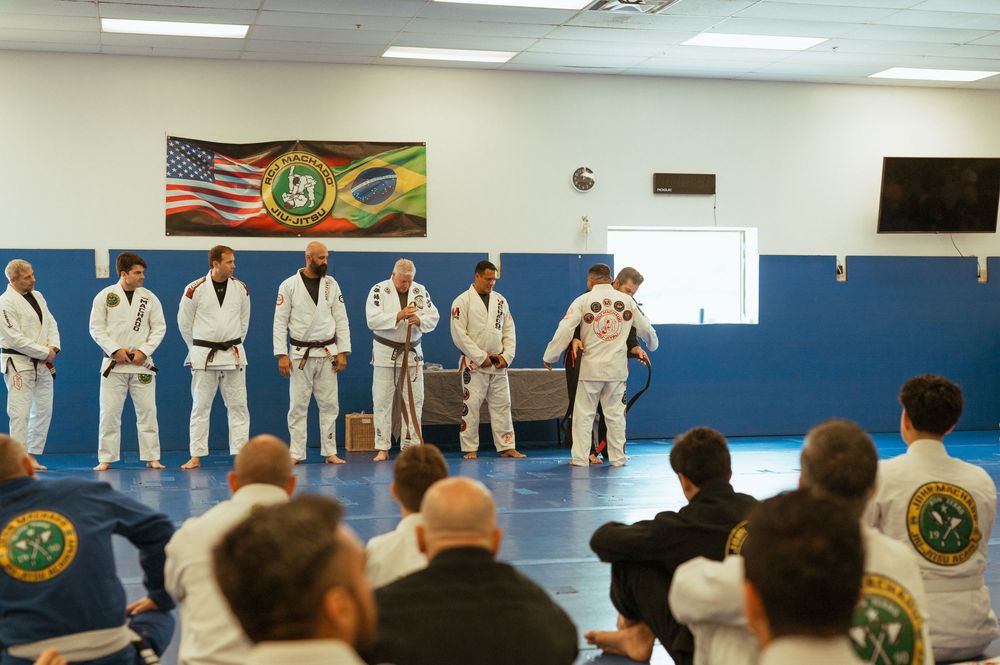 Students line up in white martial arts uniforms during a class at a dojo with colorful wall decorations.