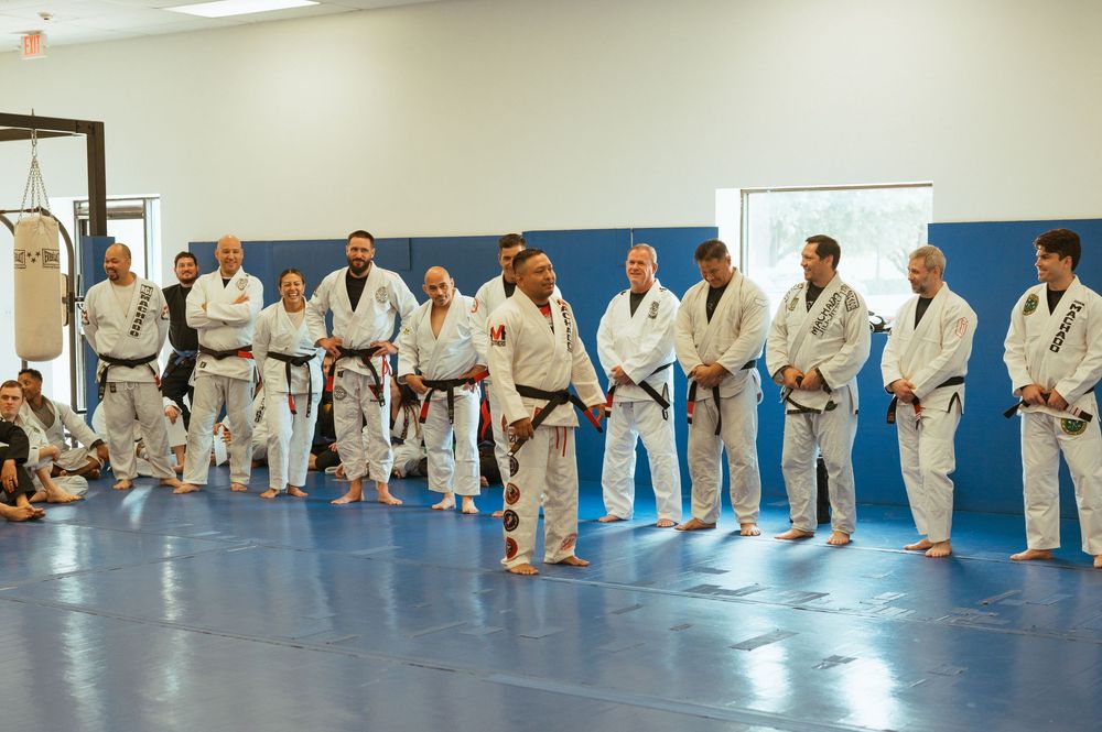 Students in white uniforms line up on a blue mat during a martial arts class instruction session.