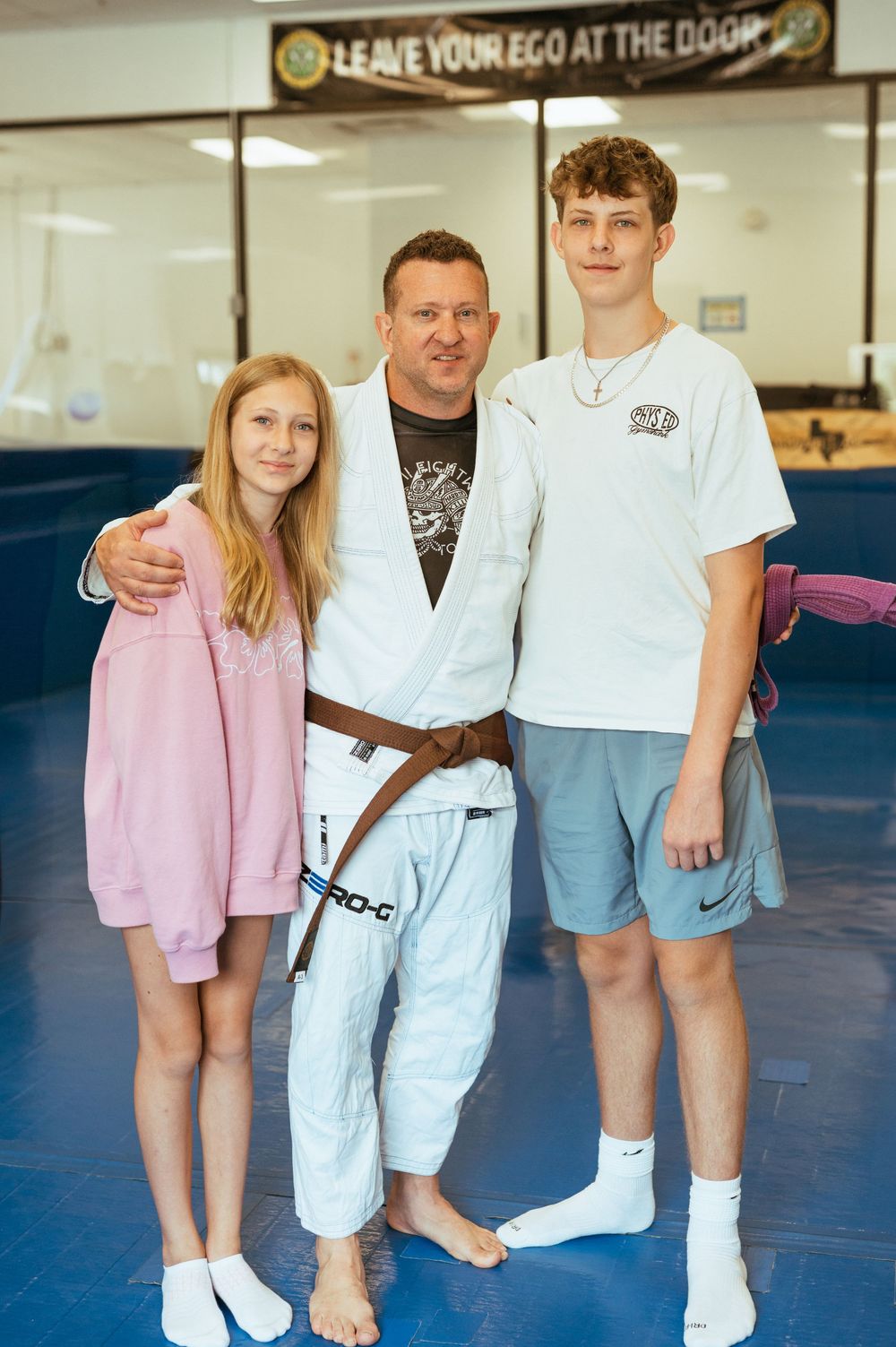 Multiple people in martial arts attire pose together on blue practice mats during a karate class.