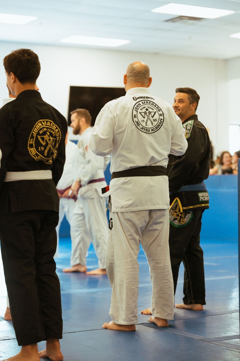 Martial arts students in white and black uniforms practicing on blue mats during a training class.