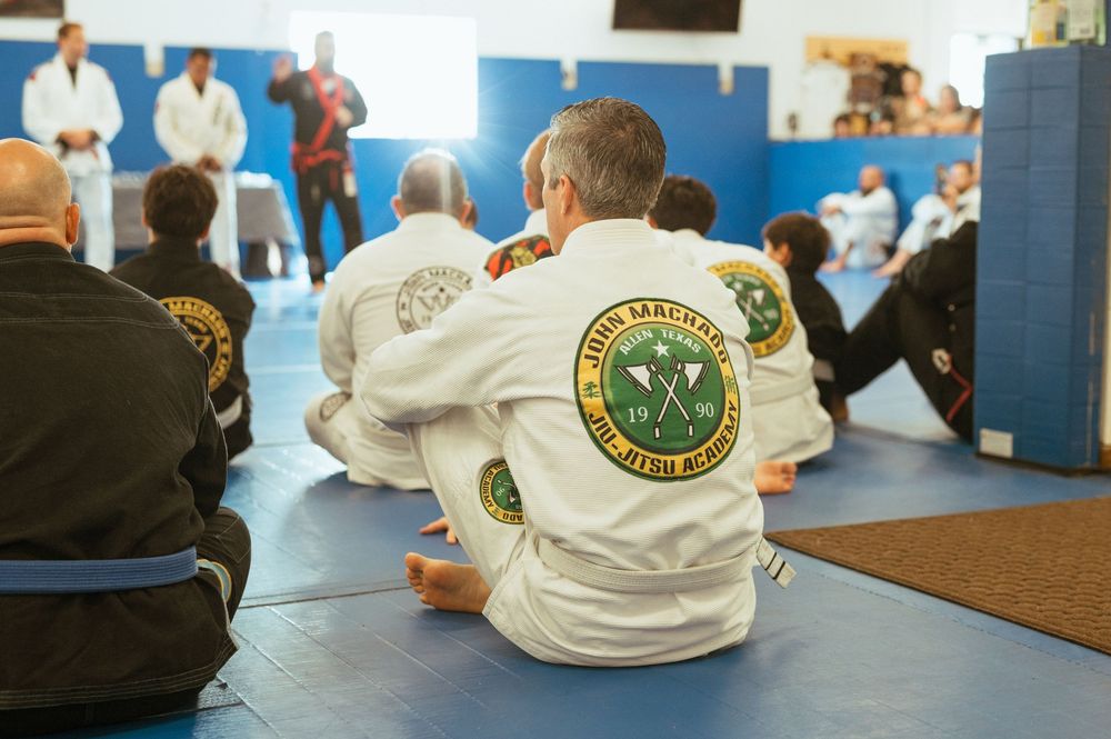 Martial arts students in white uniforms practicing during a training session on blue mats in a bright dojo.