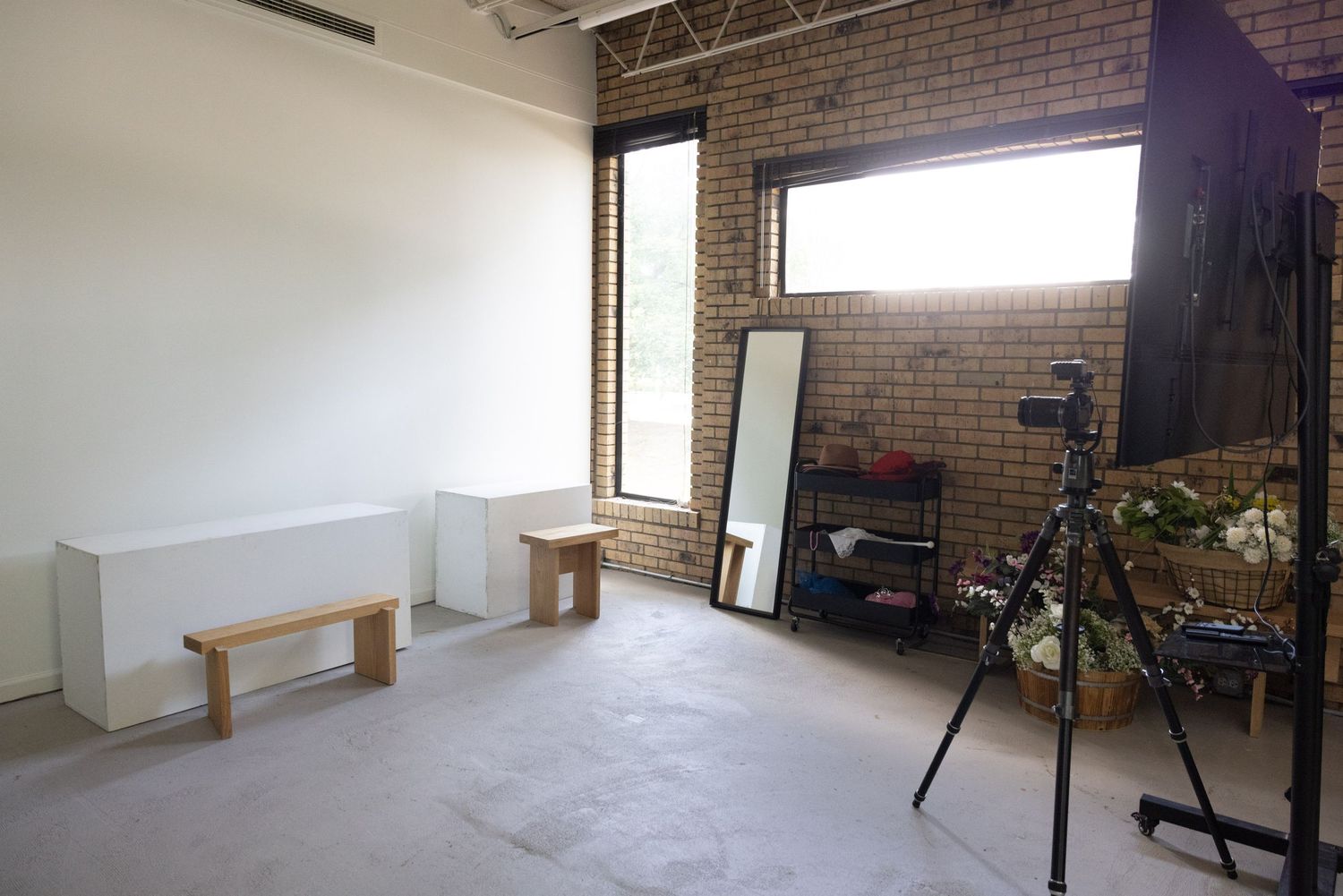 A minimalist photography studio space with exposed brick walls, a standing mirror, and a tripod setup on concrete floors.