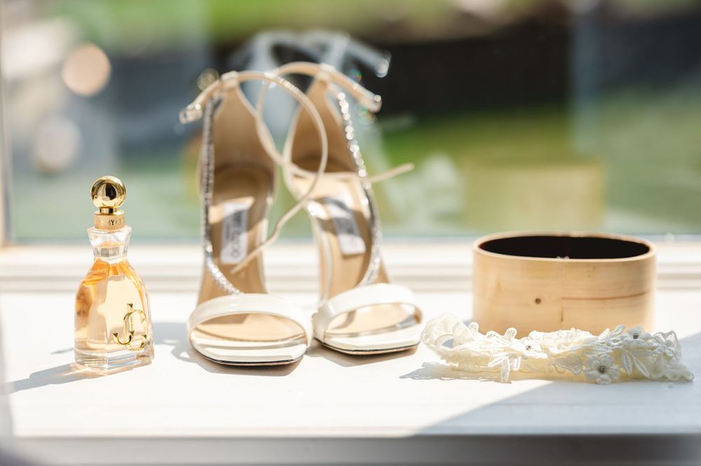 Wedding accessories including perfume, heels and jewelry box arranged on white surface. Hudson Valley wedding
